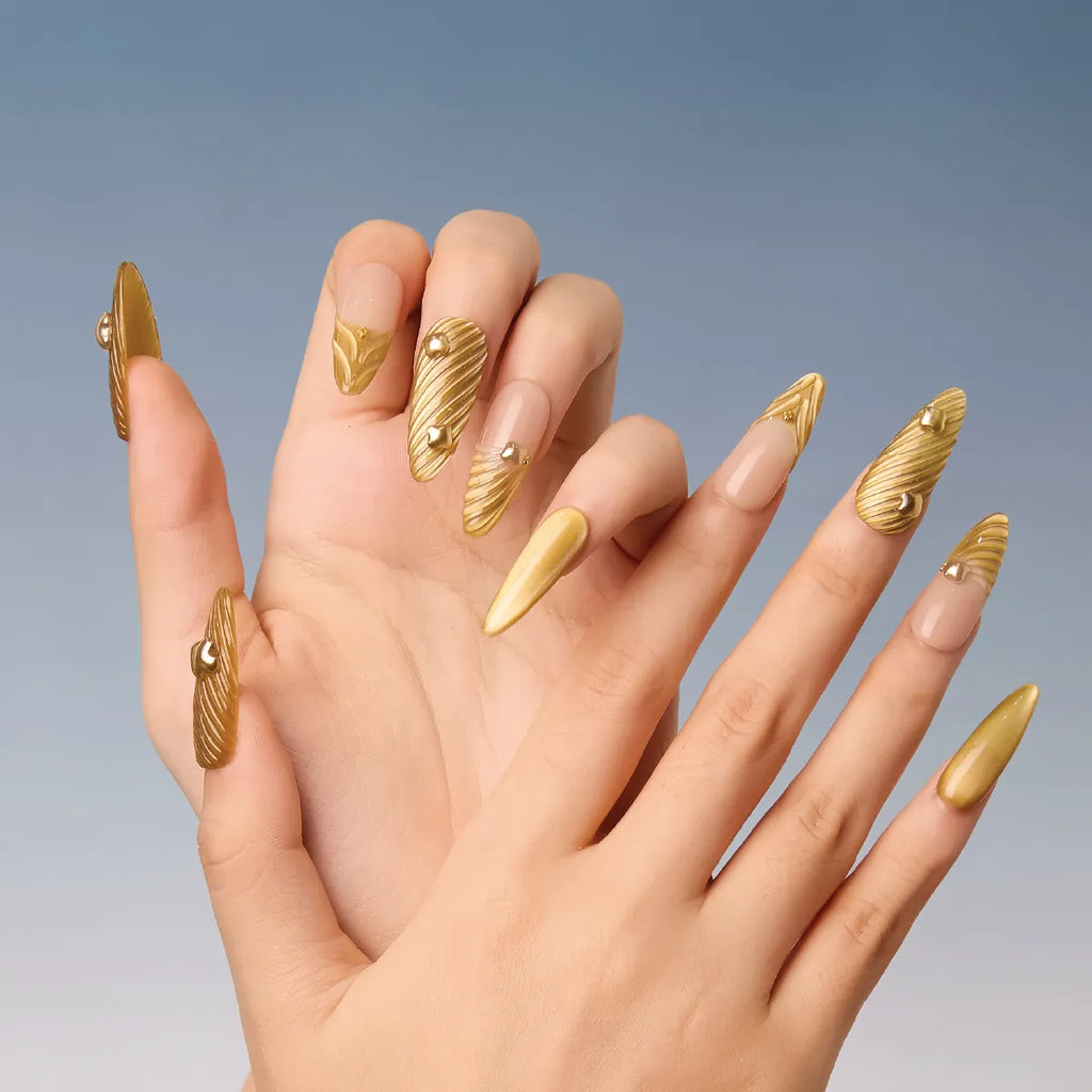 Chapter Gold 3D press-on nails (almond shape, long length) with gold 3D swirls and small gems, displayed on hands against a blue gradient background.