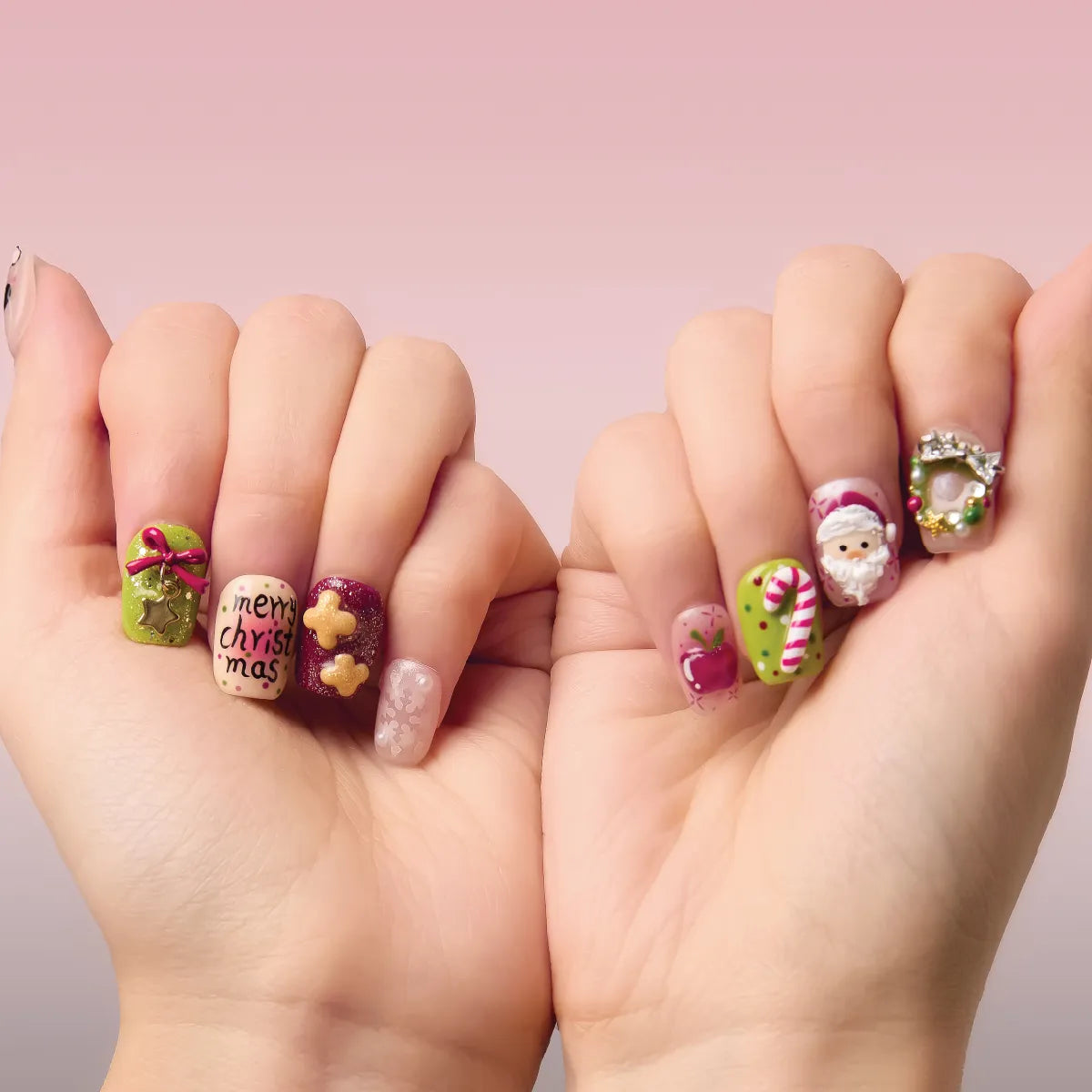 Close-up of two hands holding Christmas Sonata 3D square short press-on nails, showcasing festive designs: "merry christmas" text, bows, stars, gingerbread, Santa, candy canes, and wreaths, against a soft pink background.