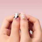 Christmas Sonata 3D square short press-on nails on a hand. Left nail: panda in chef hat with pink accents; right nail: white design with gold stars/sparkles. Soft pink background.