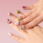 A hand showcases square 3D press-on nails from the Christmas Sonata collection, featuring festive designs: Santa, candy cane, gift box, gingerbread, wreath, and "Merry Christmas" text, set against a soft pink background.