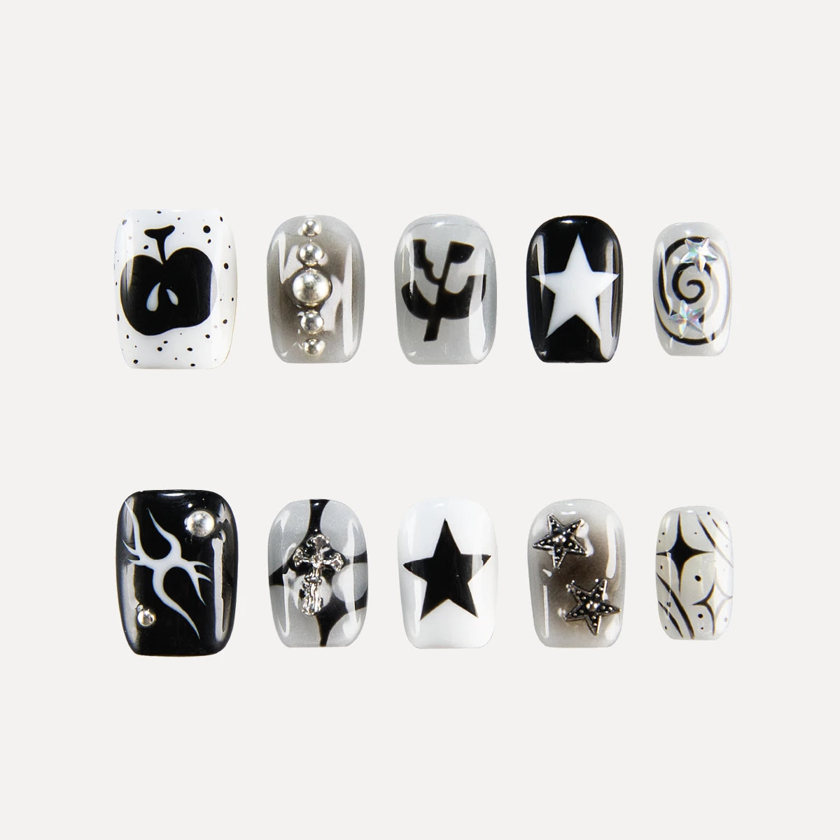 Image of the "Astro Courier" 3D press-on nail collection, featuring ten square-shaped, short nails with monochromatic (black, white, silver) designs—including stars, a skull, swirls, leaf motifs, and 3D embellishments like beads/rhinestones—arranged in two rows of five.