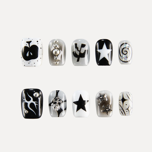 Image of the "Astro Courier" 3D press-on nail collection, featuring ten square-shaped, short nails with monochromatic (black, white, silver) designs—including stars, a skull, swirls, leaf motifs, and 3D embellishments like beads/rhinestones—arranged in two rows of five.
