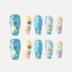 Image of 3D press-on nails from the "Candy Night" collection, featuring coffin-shaped, medium-length nails with vibrant, playful designs. Two rows of five nails each showcase colorful patterns: blue glitter bases with yellow stars and red/pink polka dots; yellow-and-white nails with "LOVE" text and a yellow circular accent; blue nails with abstract pink shapes and red dots; nails with "Los for Paris" text in silver on a blue/pink background; and yellow nails with pink shapes and blue glitter accents.