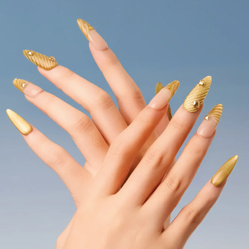 Chapter Gold 3D press-on nails (almond shape, long length) with gold textured designs and small decorative accents, displayed on a hand against a blue background.