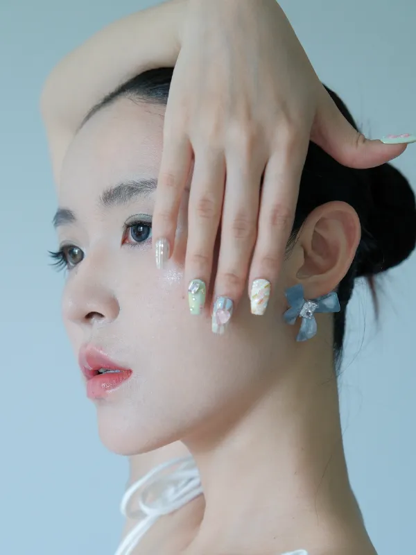 A portrait of a model wearing blue 3D butterfly-themed press-on nails near her face.