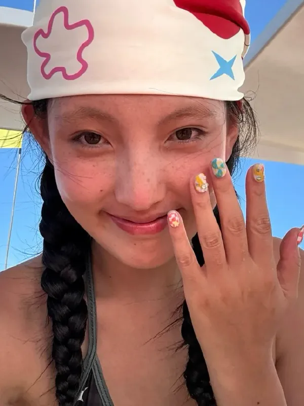 A smiling customer showing colorful press-on nails while outdoors in the sunlight.