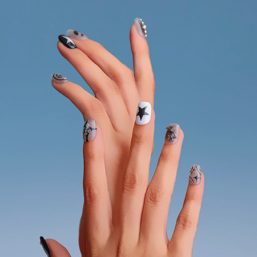 Hand wearing LOST in PARK Astro Courier short square press-on nails with black-and-white star graphics and silver accents against a soft blue background.
