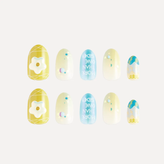 Flat lay of yellow and blue decorative press-on nails with 3D flower charm and gradient patterns.