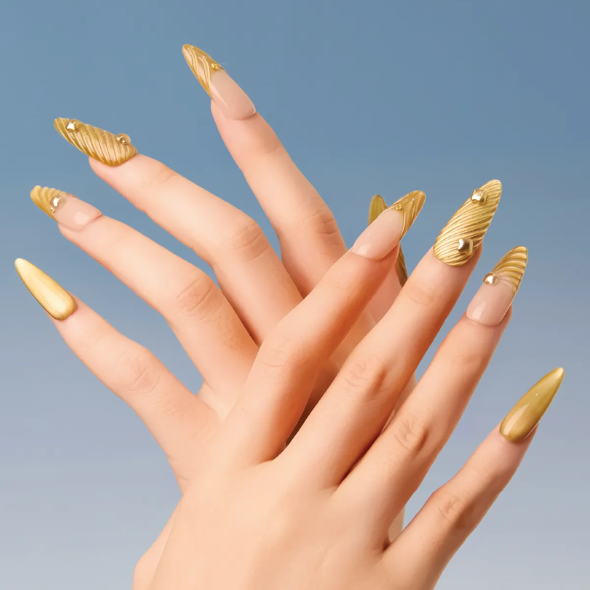 Model hands displaying gold ribbed long almond press-on nails styled with nude negative space.