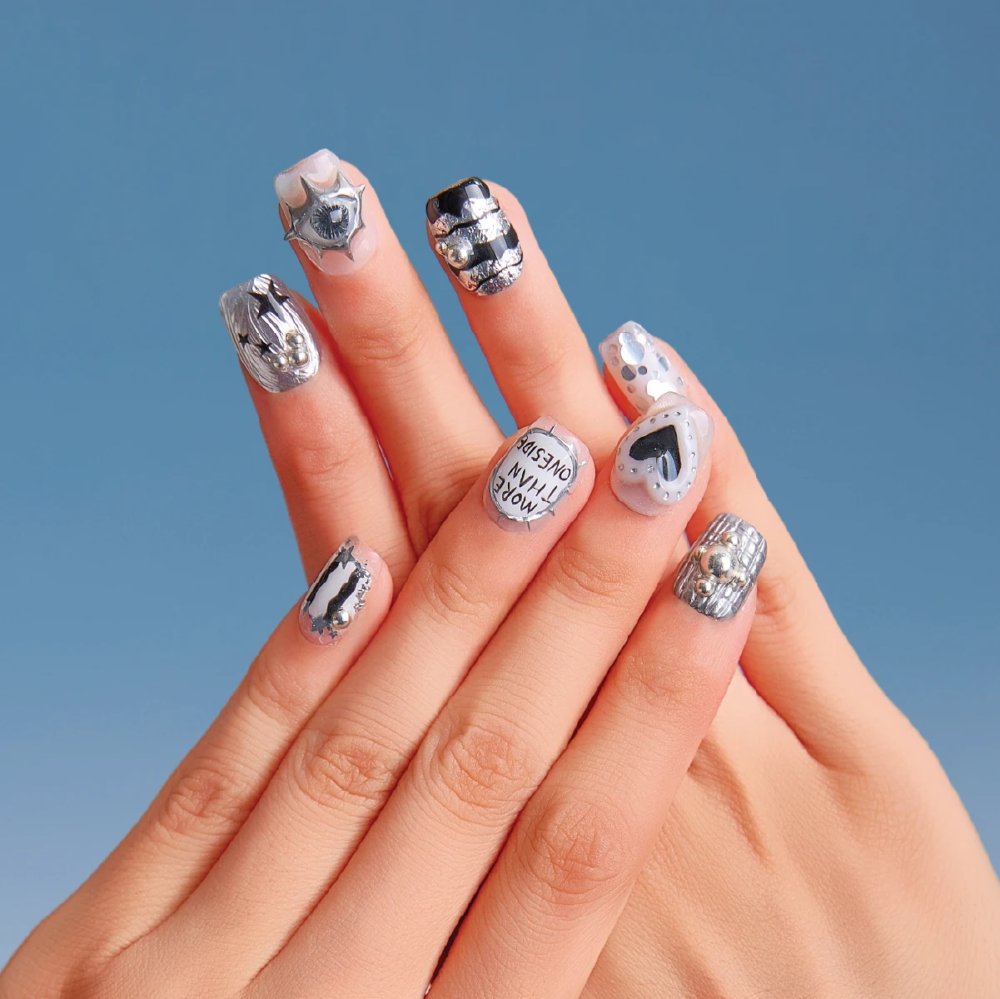 Close-up of both hands wearing Chrome Vision short square nails featuring black-silver patterns, text details, heart design, and metallic studs.