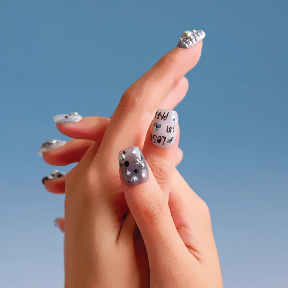 Back-of-hand shot showing Chrome Vision press-on nails with silver chrome textures, star patterns, and raised bead accents.