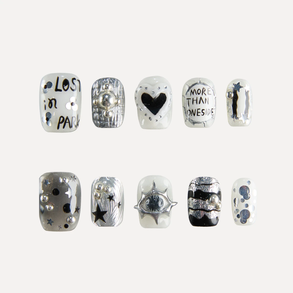 Flat lay of 10 Chrome Vision short square press-on nails featuring silver chrome textures, handwritten text graphics, heart motif, star accents, and 3D metallic studs.