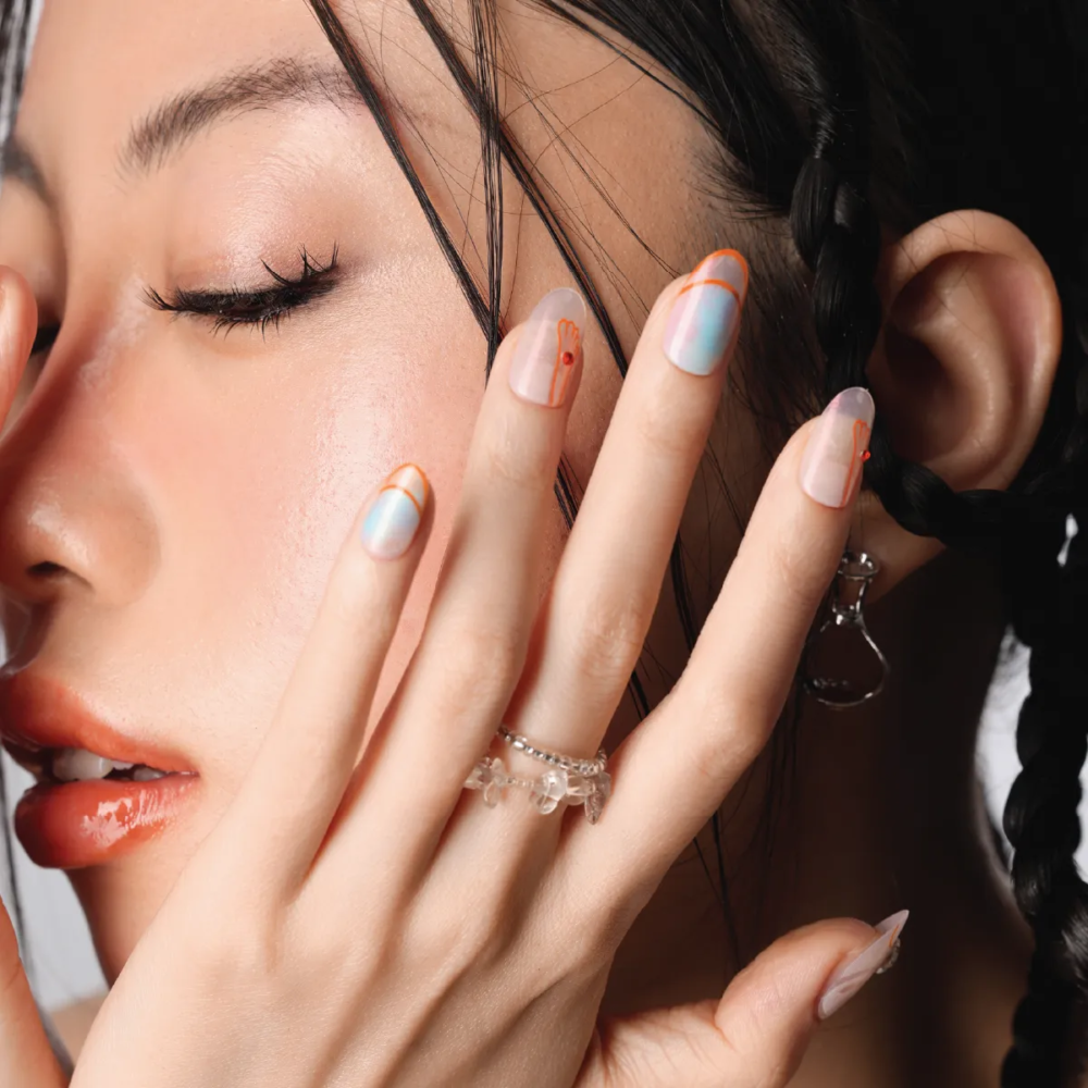 Model beauty shot highlighting the “Crystal Mist” nails, featuring iridescent pastel tones and bold orange outlines against natural skin texture.