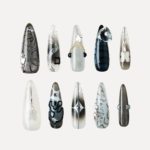 Flat lay of Cyber Pulse long stiletto press-on nails arranged in rows with metallic gradients, chrome 3D pieces, and futuristic black-silver designs