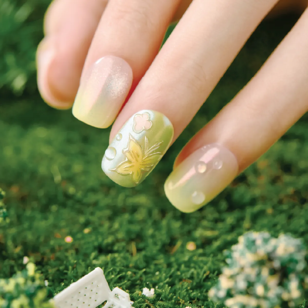 Hand wearing Dewy Garden press-on nails featuring yellow-green gradients, embossed butterfly design, and 3D dewdrop accents