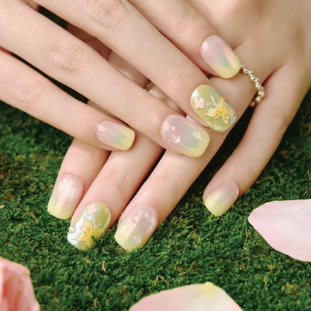 Soft gradient green and pink press-on nails with embossed butterfly and dewdrop details showcased on natural grass background