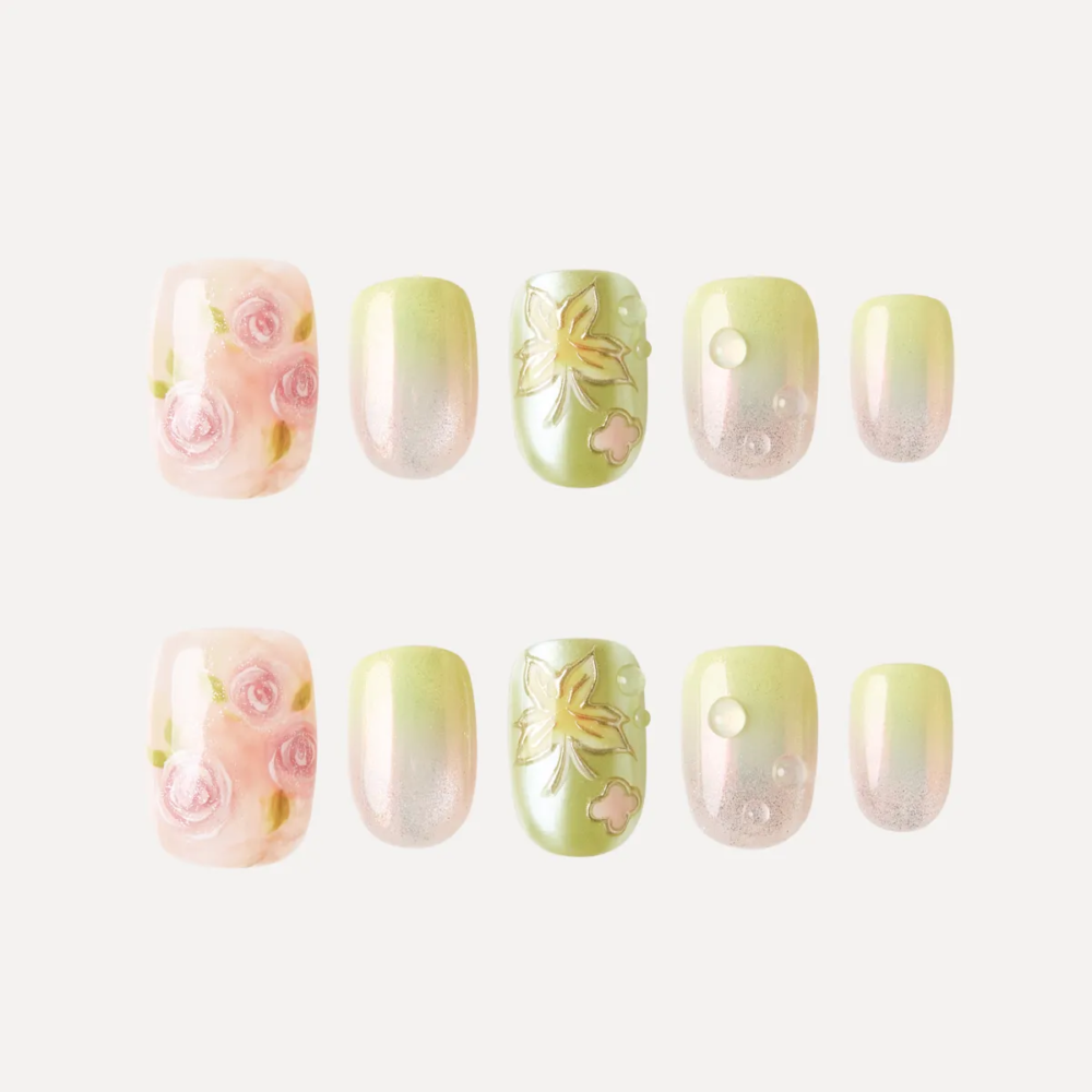 Flat lay of Dewy Garden press-on nail tips featuring pink roses, green floral embossing, and shimmering gradient designs