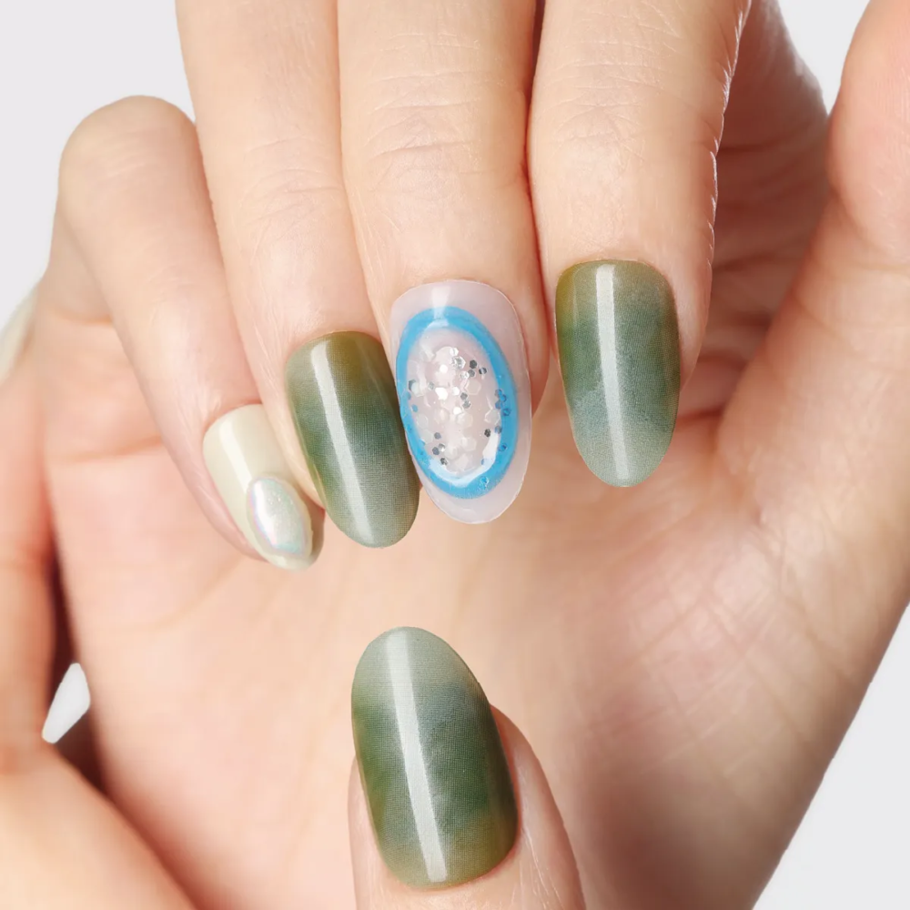 Close-up of green gradient press-on nails featuring blue jelly oval detail with silver glitter