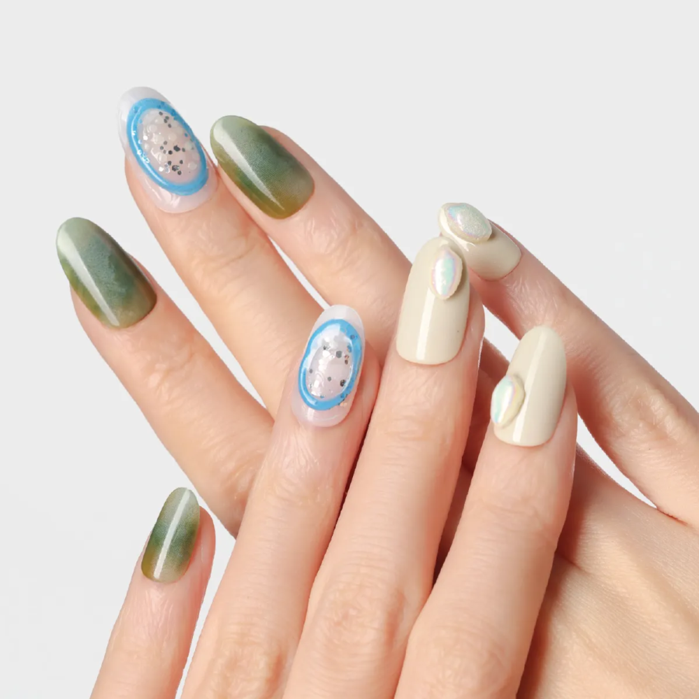 Hand displaying emerald green gradient nails mixed with nude pearl accent nails and blue jelly oval design