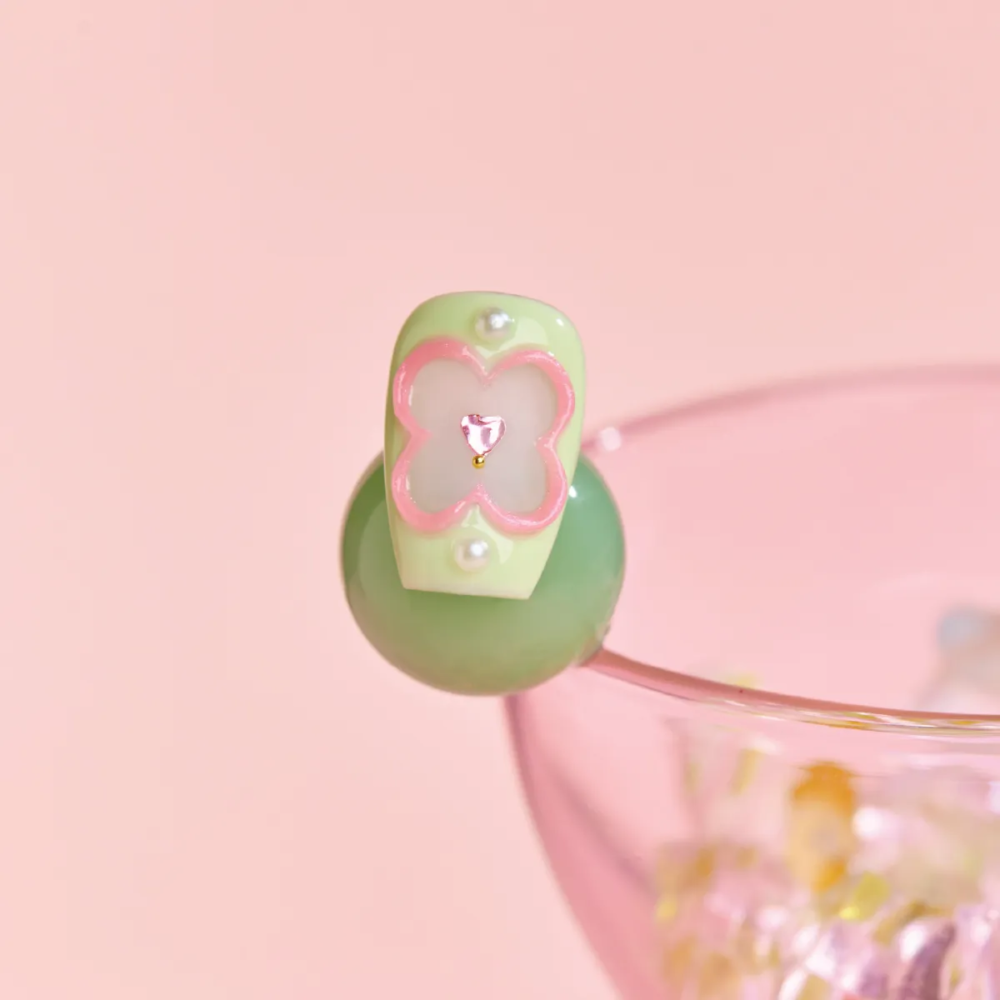 Macro shot of green press-on nail with pink outlined flower and pearl details