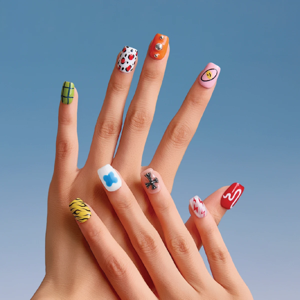 Both hands showing off mismatched press-on nails with eclectic cartoon-inspired patterns