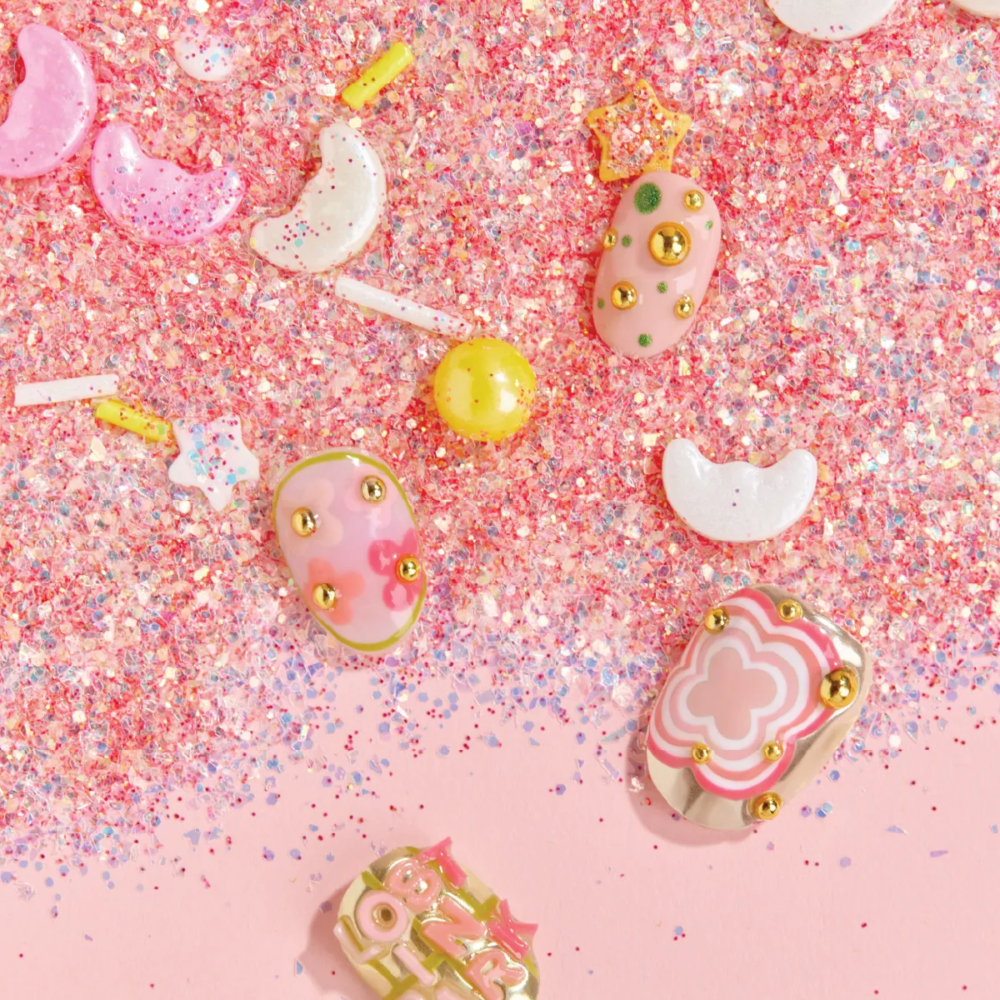 Flat lay of colorful press-on nails on pink glitter background with candy and moon-shaped decorations