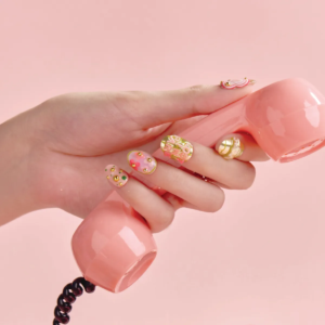 Hand with vibrant pink and gold press-on nails holding a vintage pink telephone handset