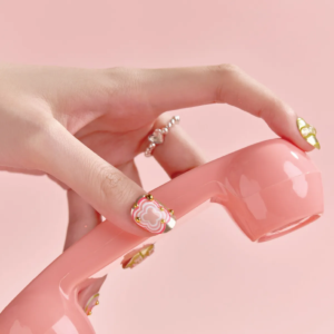 Close-up of thumb wearing pink patterned press-on nail with golden beads, holding pink phone