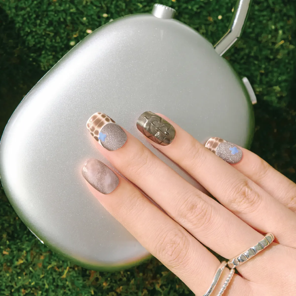 Hand wearing LOST in PARK “Mocha Mirage” press-on nails – glittery taupe and metallic designs