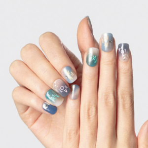Close-up of hands wearing gradient blue and green press-on nails with words like “LOVE” and “FREE”