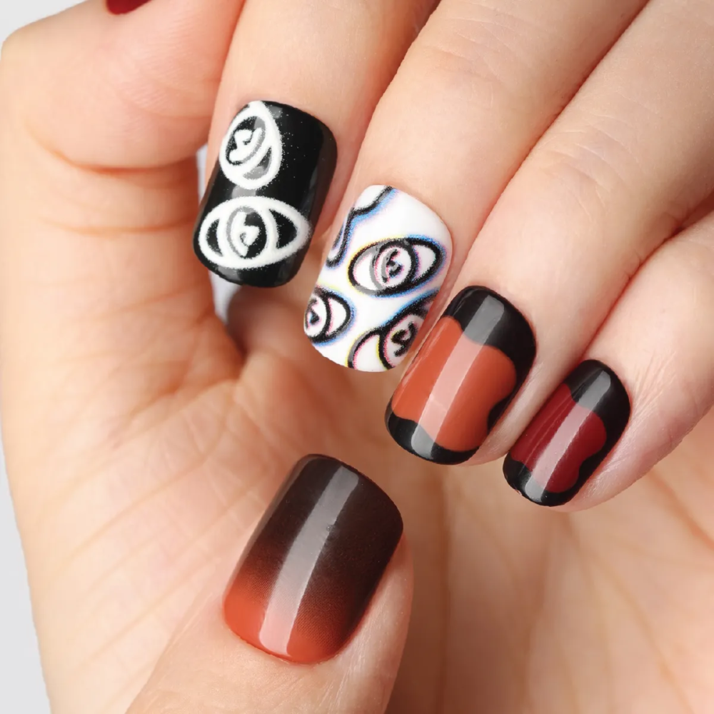 Close-up of press-on nails in deep red and black tones with abstract white eye illustrations and gradient effects on fingers.