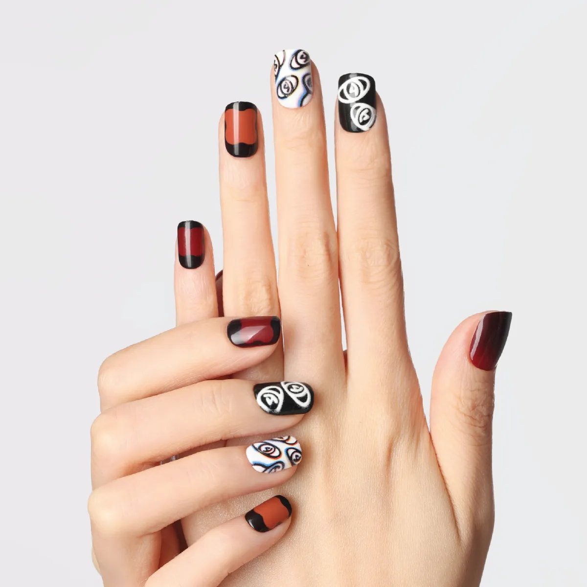 plum rhapsody press-on nails in deep red and black tones with abstract white eye illustrations and gradient effects on fingers.