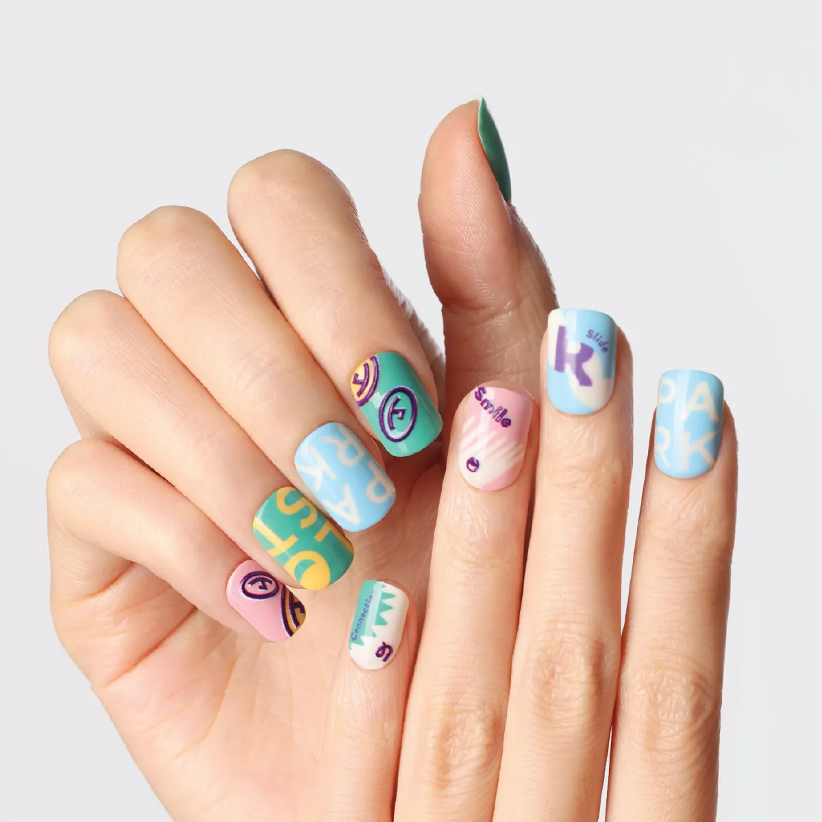 Hands showing colorful Riotous Paradise press-on nails with playful smiley and text designs