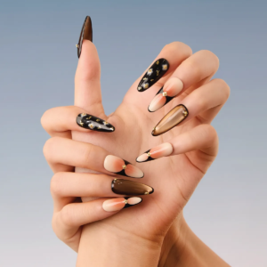 Close-up of hand posing with long almond press-on nails featuring black edges, nude gradients, and gold accents.