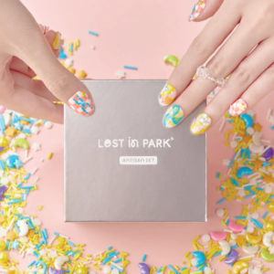 Hands holding LOST in PARK silver nail box with Artisan Set label, surrounded by colorful candy sprinkles.