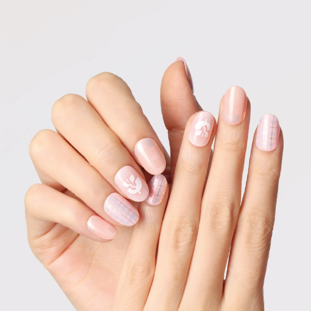 Front view of overlapping hands showing full set of pink press-on nails with plaid and shimmer design.