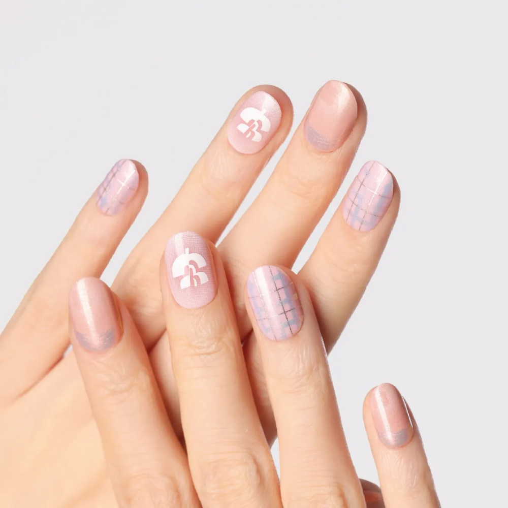 Hand pose showcasing pastel press-on nails with holographic shine and graphic white floral logo.