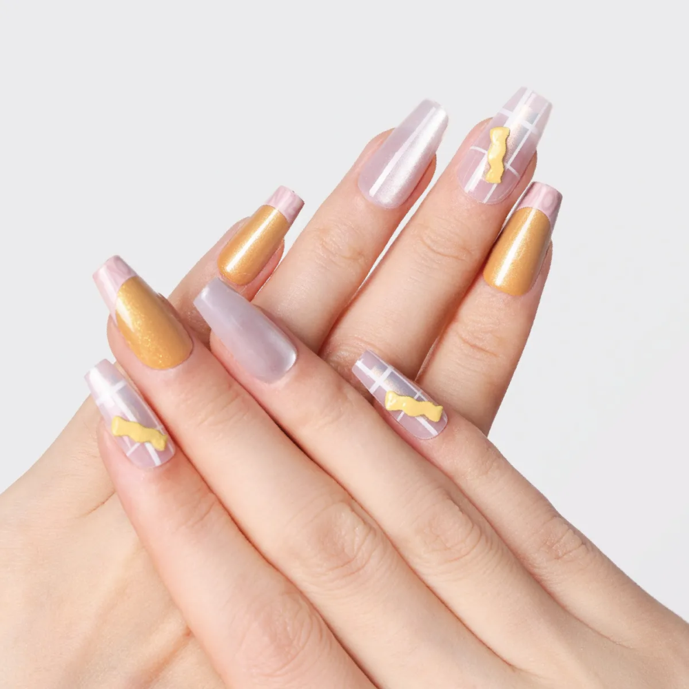 Hand pose showing long almond press-on nails in gold, pearl white, and pink grid patterns with 3D yellow candy embellishments.