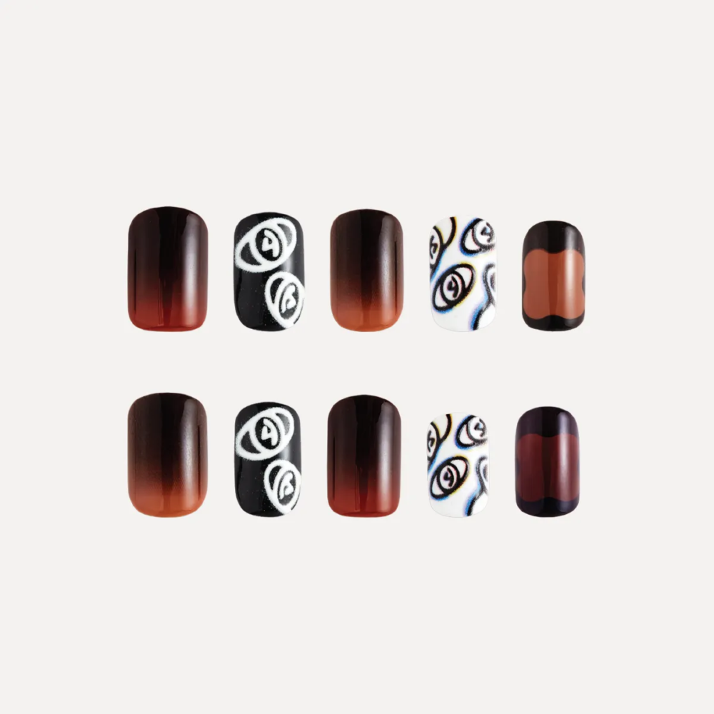 Flat lay of ten press-on nail pieces in a red-black gradient with black and white eye motifs and layered transparent panels.