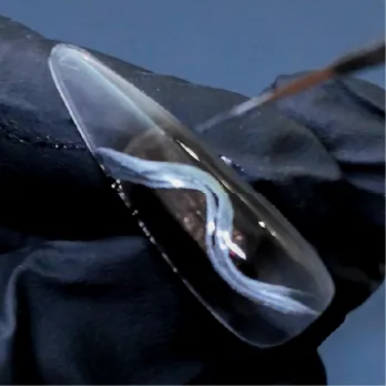 Hand painting white ripple texture onto a clear sculpted press-on nail.