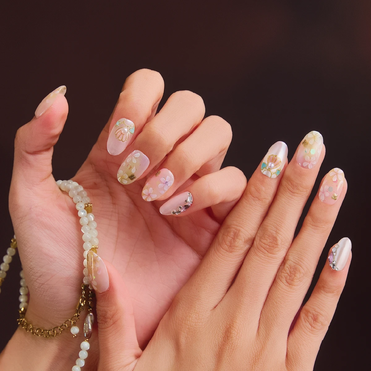 Short oval press on nail set styled on hands with floral pastel design