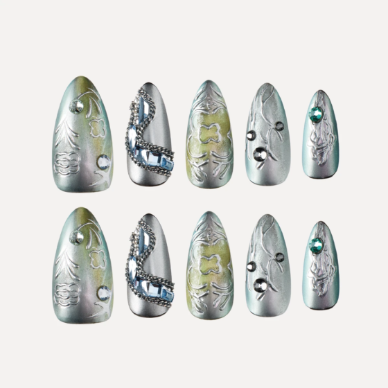 Medium almond press on nails flat lay in silver green tones with embossed patterns chains and gemstone details