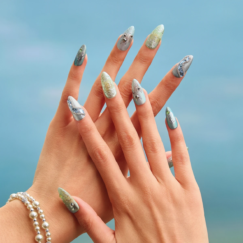 Medium almond press on nails worn on hands with silver green metallic finish and sculpted details